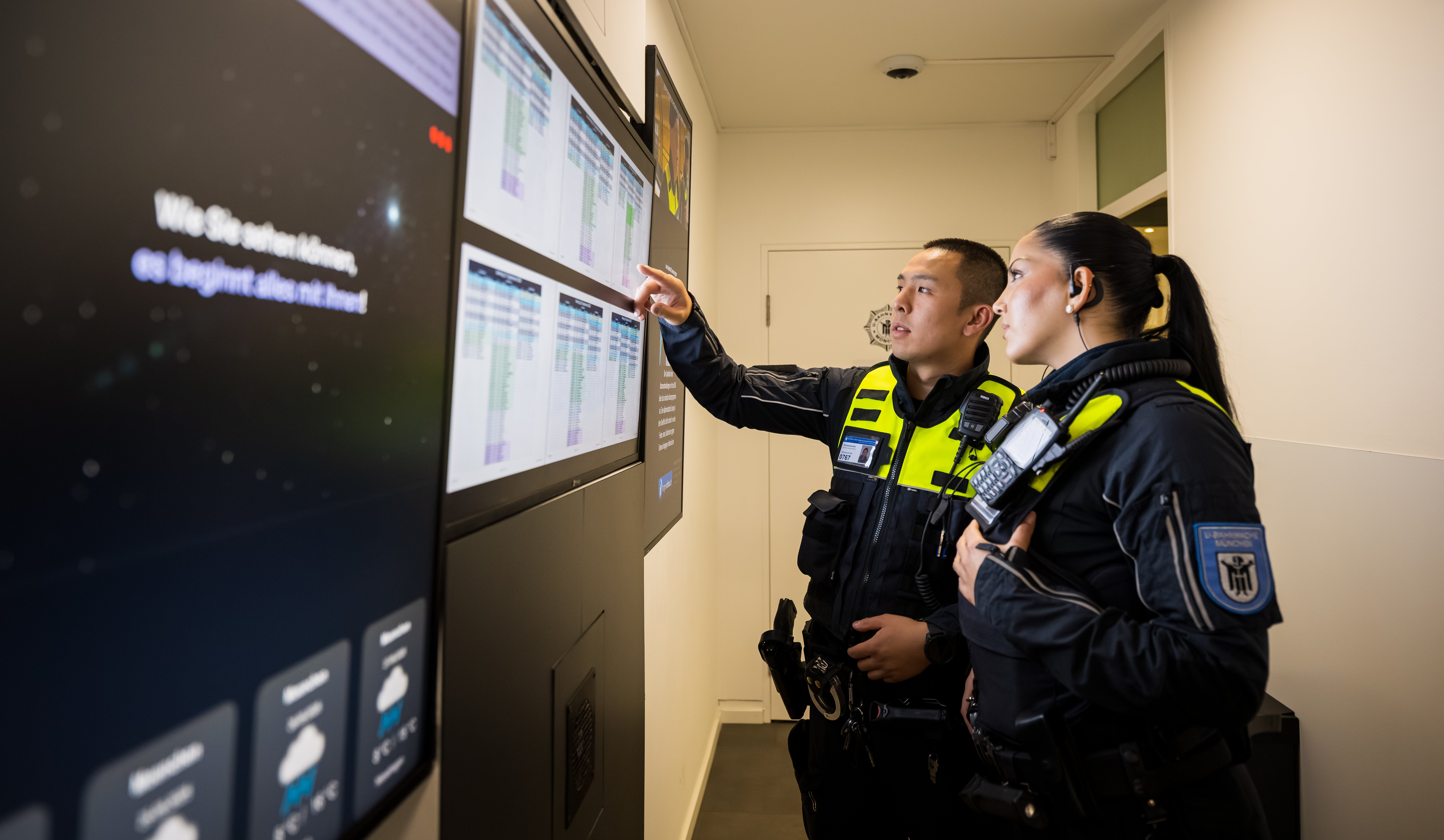 A female and a male Münchner U-Bahnwache guard looking at data from Securitas on big screens.